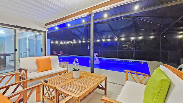 A modern indoor pool area with a glass wall, wooden furniture, and a swan decoration. - Serene Pool Oasis Tampa Vacation Villa (Tampa)