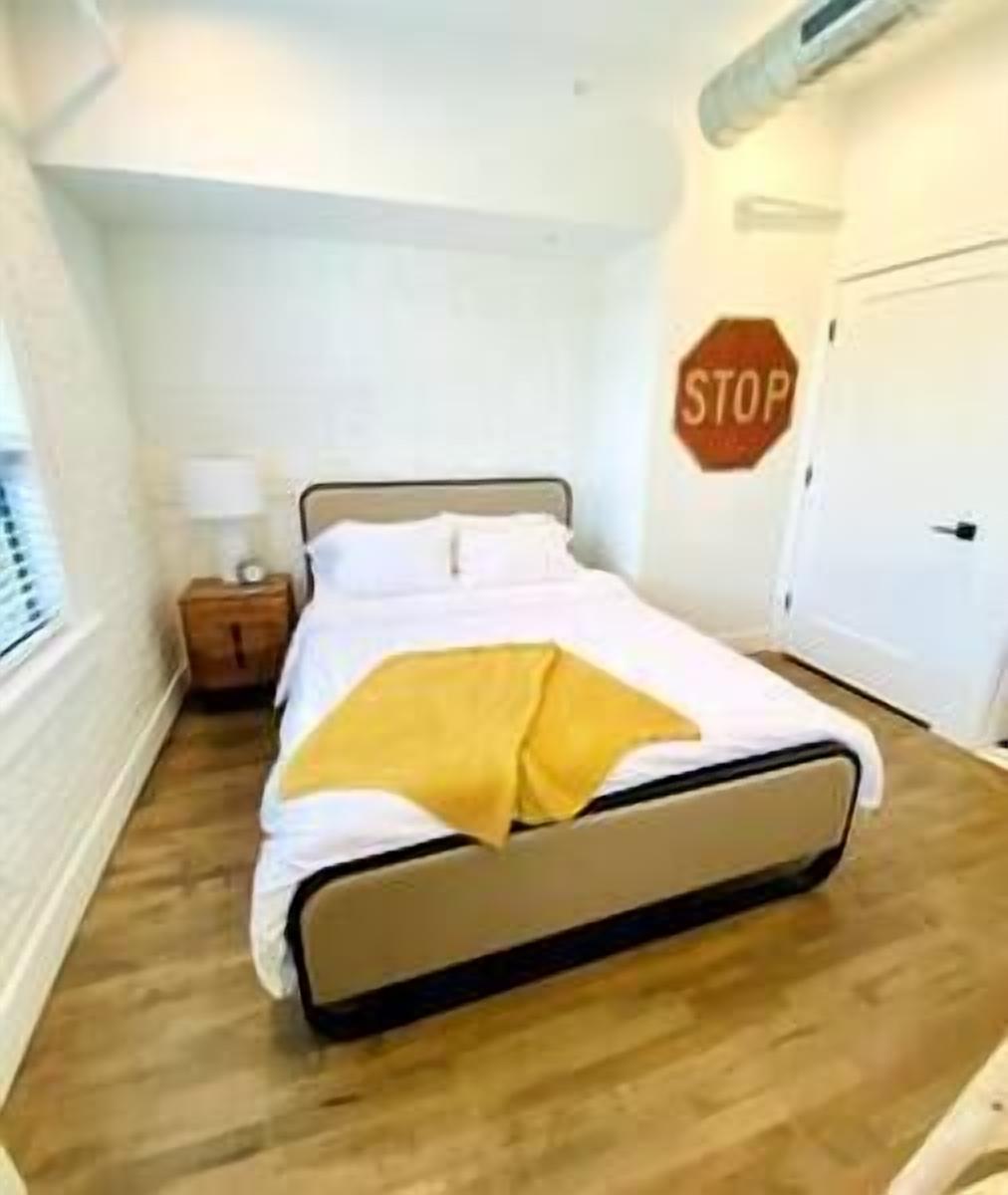 Un dormitorio con una cama, una mesita de noche, un letrero de alto en la pared y una puerta.