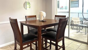 A dining area with a wooden table and four chairs, a white curtain, and a view of the outside.