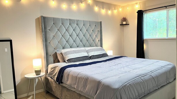 A bedroom with a tufted headboard, a bed with a grey duvet, bedside lamps, and string lights.