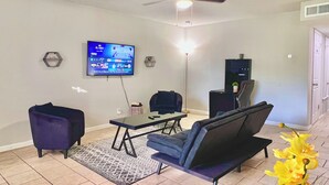A living room with a TV, two chairs, a coffee table, and a small plant.