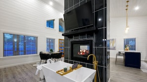 A modern living room with a large flat-screen TV, a fireplace, and a white bathtub. - Sauna, Bar, Big Patio, Hot Tub, Fire Pit & Pets (Broken Bow)
