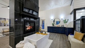 A modern living room with a fireplace, a large white bathtub, and a cozy seating area. - Sauna, Bar, Big Patio, Hot Tub, Fire Pit & Pets (Broken Bow)
