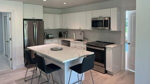 Una cocina moderna con armarios blancos, electrodomésticos de acero inoxidable y una isla de mármol con taburetes.
