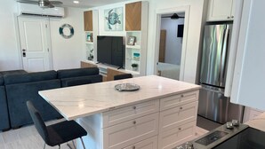 Una cocina moderna con una isla central, electrodomésticos integrados y una zona de estar con sofá y taburetes de bar.