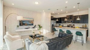 A modern living room with a sofa, chairs, a coffee table, and a TV mounted on the wall. - 5BR Villa w/ Private Pool | Disney Themes (Davenport)