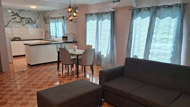 Ein Wohnzimmer mit einer Couch, einem Hocker und einem Essbereich mit Stühlen und einem Tisch.