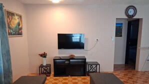Ein Wohnzimmer mit Flachbildfernseher, einer Couch, einem kleinen Tisch mit einer Vase und einem gemusterten Teppich.
