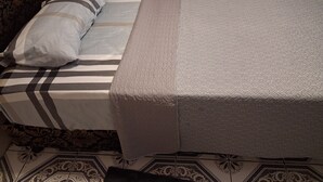 Ein Bett mit gemustertem Überwurf und Kissen, ein Kopfteil mit floralem Design sowie ein gemusterter Boden.