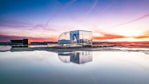 A modern glass dome structure with a reflective surface, situated on a reflective water body, with a clear sky in the background.
