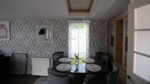 A dining area with a table, four chairs, a vase with flowers, a radiator, and a window with blinds. - No.16 Nursery park caravan site (Brechin)