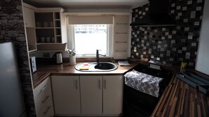 A compact kitchen with a built-in stove, a sink, and a window providing natural light. - No.16 Nursery park caravan site (Brechin)