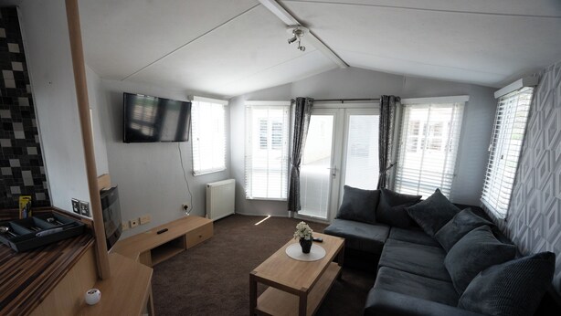 A modern living room with a sofa, a coffee table, a TV, and a fireplace. - No.16 Nursery park caravan site (Brechin)