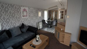 A modern living room with a grey sofa, a wooden coffee table, and a TV stand. - No.16 Nursery park caravan site (Brechin)