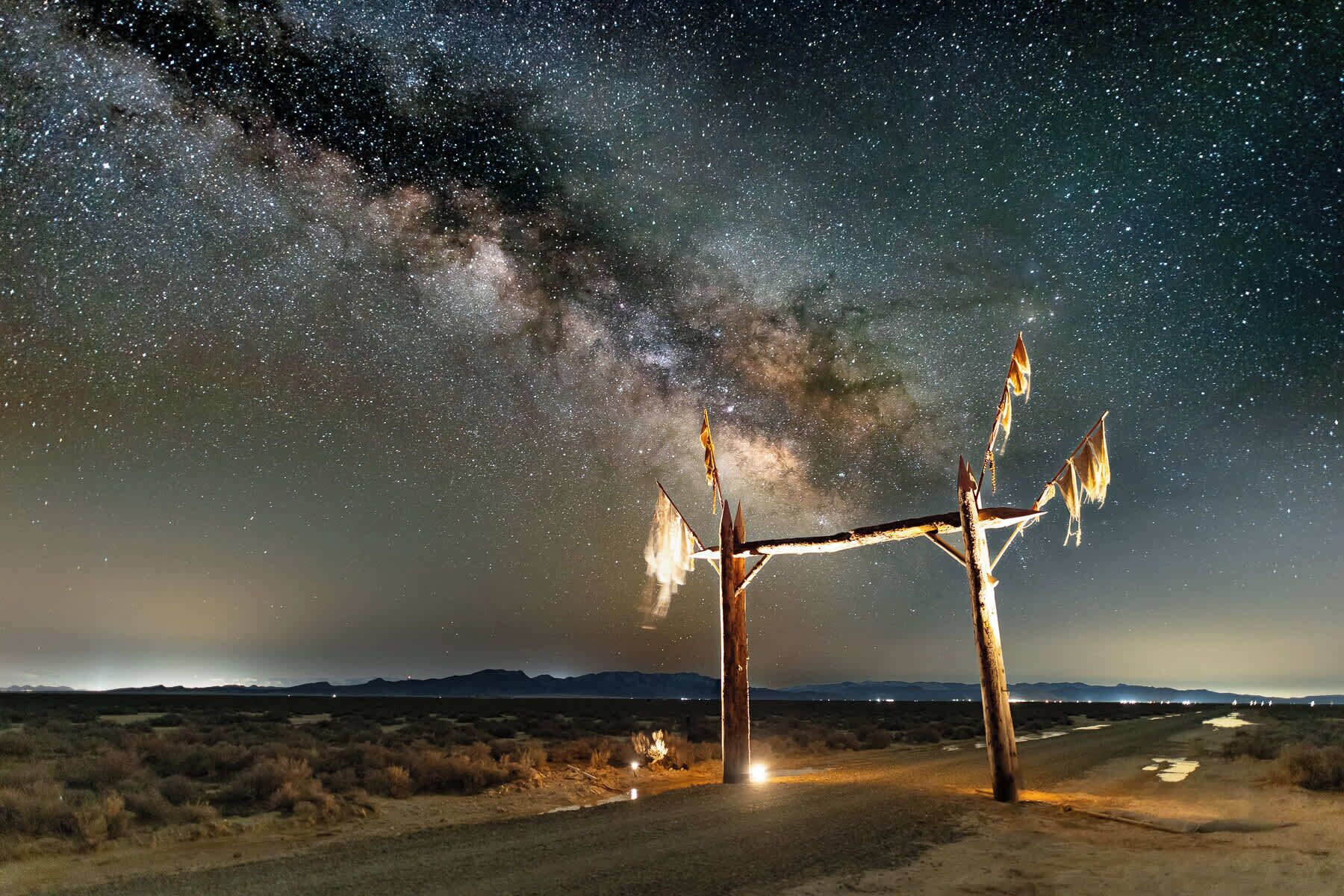 Un paysage désertique avec une structure en bois surmontée d’un toit en forme d’étoile, sous un ciel nocturne étoilé.