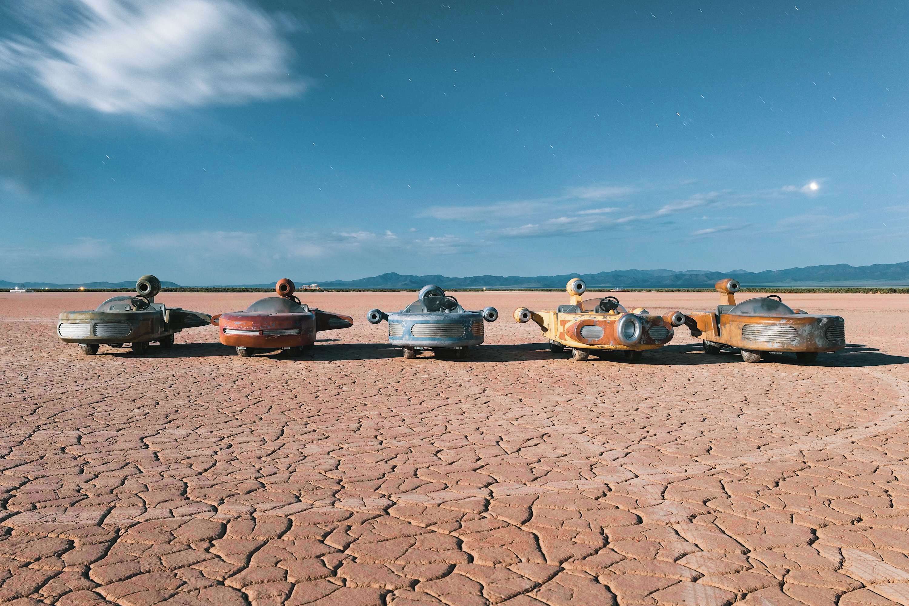 A row of vintage military tanks on a dry, cracked ground with mountains in the background.