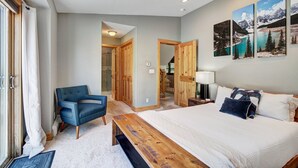Ein Schlafzimmer mit einem Bett, einem Sessel, einer hölzernen Bank, einer Tür zu einem Badezimmer und einer Wand mit drei gerahmten Bildern.