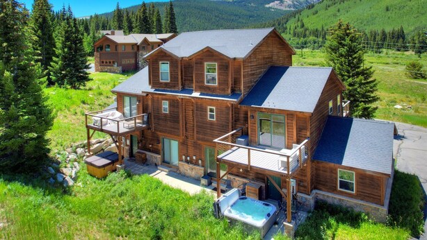 Eine große Holzhütte mit mehreren Ebenen, einem Whirlpool und einer malerischen Bergkulisse.