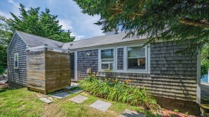 A two-story house with a sloped roof, a wooden deck, and a garden with stepping stones. - Relax at Hilltop Hideaway, Near the Shore (Dennis Port)