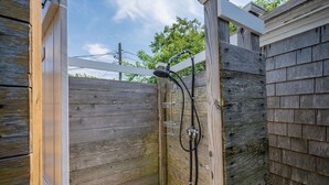 A wooden outdoor shower with a metal showerhead and hose, enclosed by a wooden fence. - Relax at Hilltop Hideaway, Near the Shore (Dennis Port)