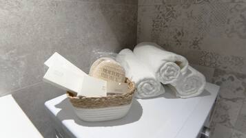 Een badkamer met een witte wastafel, een gevlochten mand met toiletartikelen, en netjes opgerolde handdoeken.