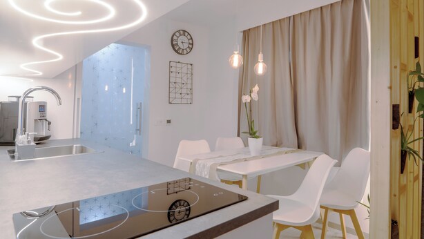 A modern kitchen with a built-in stove, a coffee machine, and a sink. There is a dining area with a table and chairs.