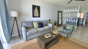 Ein Wohnzimmer mit grauem Sofa, einem Couchtisch, einer Stehlampe, einem Deckenventilator und einem dekorativen Spiegel.