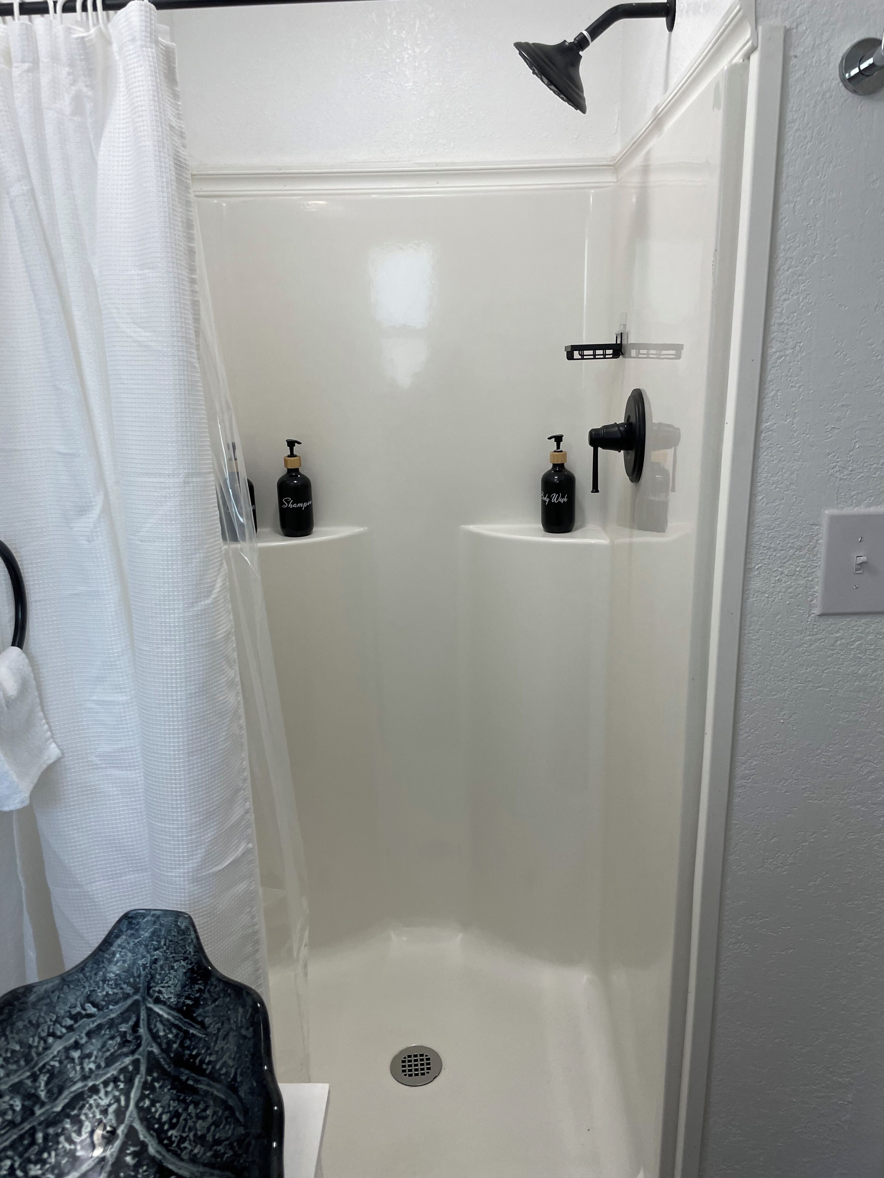 A walk-in shower with a white interior, a showerhead, and two bottles of shampoo and conditioner on the wall.