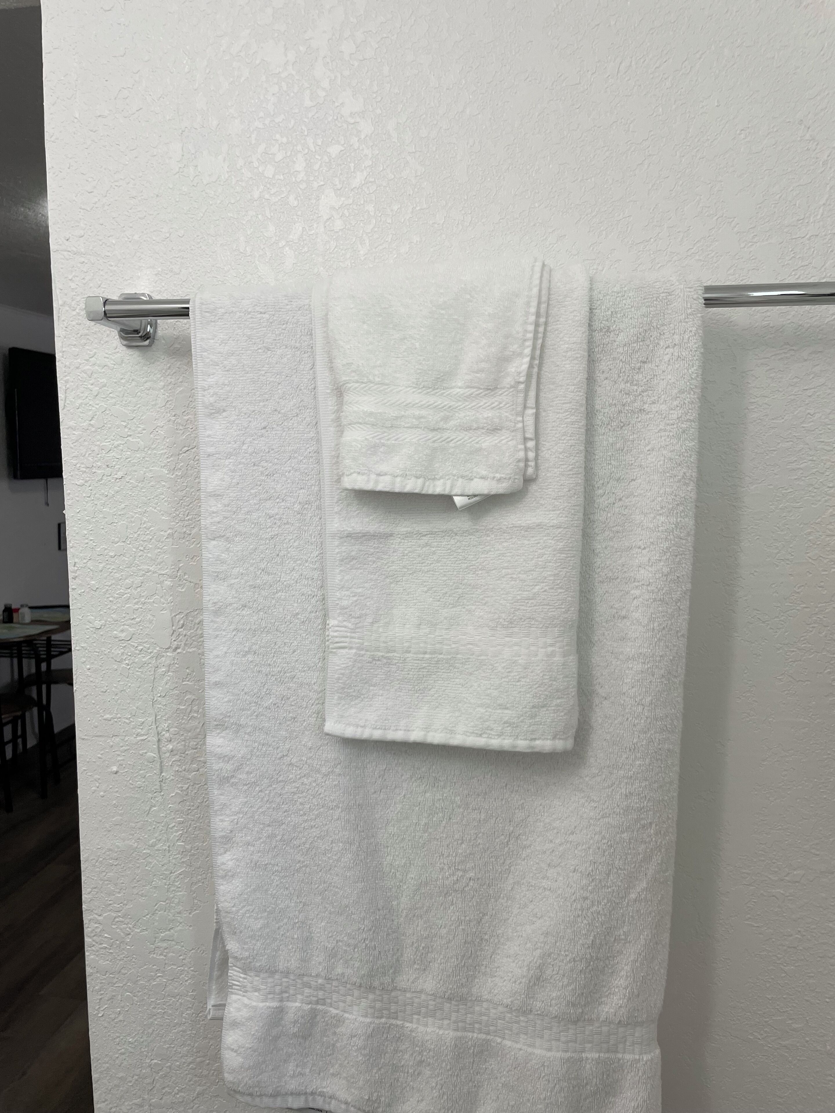 A white towel hanging on a metallic towel rack in a room with a textured white wall and a wooden floor.
