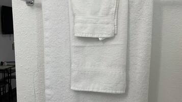 A white towel hanging on a metallic towel rack in a room with a textured white wall and a wooden floor.
