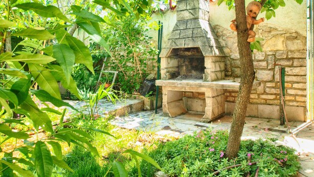 A stone-built outdoor kitchen area with a pizza oven, surrounded by lush greenery and a stone wall. - Apartment 1362/116992 (Istria - Peroj), 500m from the beach (Peroj)