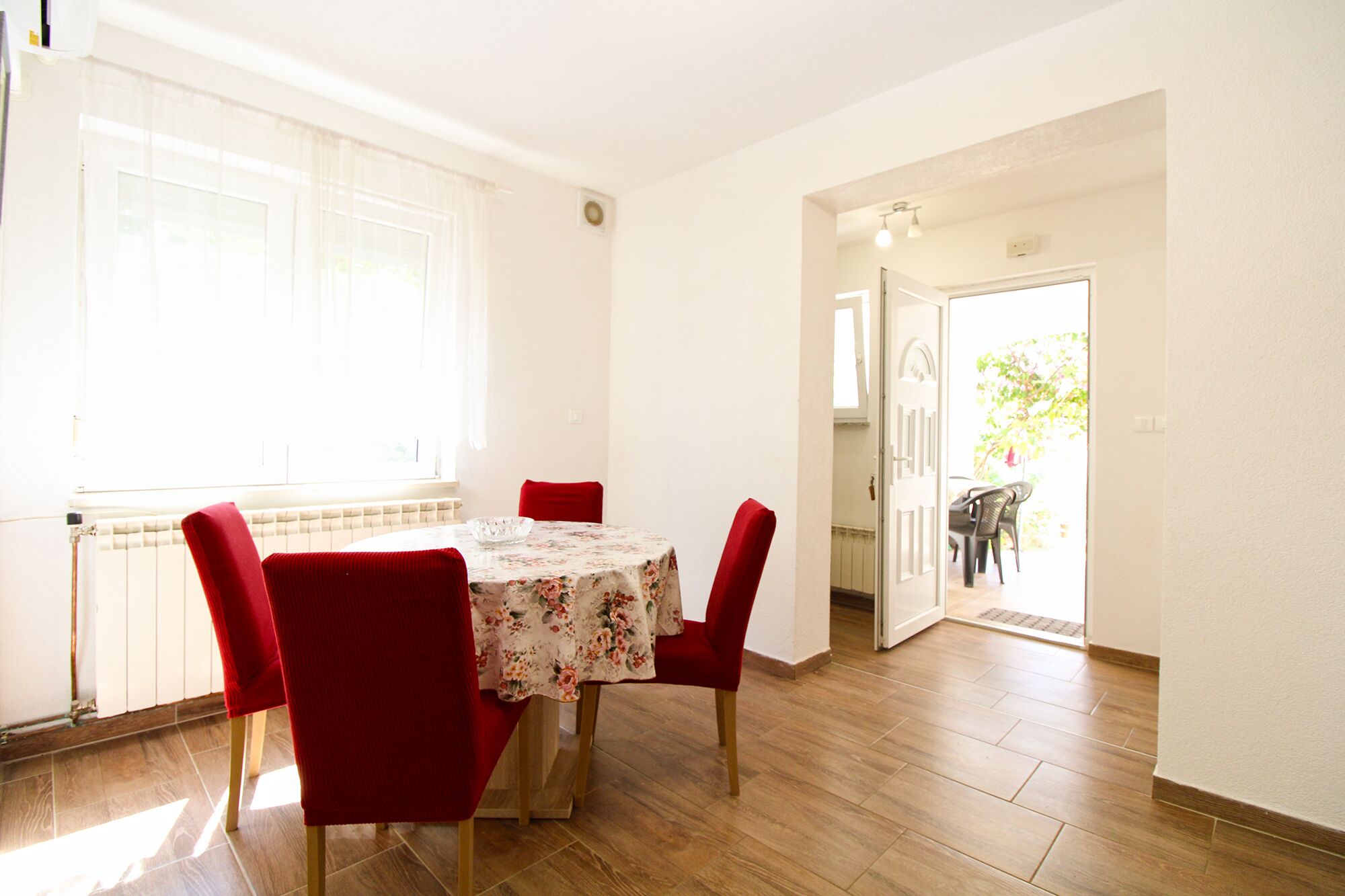 A dining area with a round table, red chairs, and a floral tablecloth.
