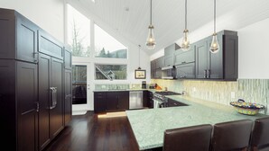 Una cucina moderna con mobili in legno scuro, un'isola verde e luci a sospensione.