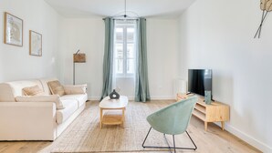 A modern living room with a sofa, a coffee table, a chair, a TV, and a window with curtains.