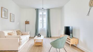 Un salon moderne avec un canapé, une table basse, un fauteuil, un téléviseur et une fenêtre avec des rideaux.