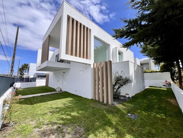 A modern two-story house with a flat roof, large windows, and a well-maintained lawn.