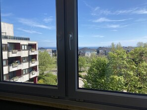 A view from a window of a building with multiple balconies, a clear sky, and greenery.