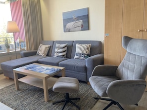 A living room with a grey sofa, a wooden coffee table, a grey armchair, and a painting of a seagull on a boat.