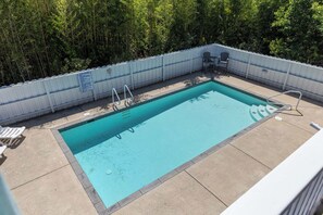 Ein rechteckiger Pool mit weißem Zaun und Metallhandläufen, umgeben von einer Betonplattform.
