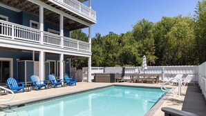 Une piscine avec des chaises bleues, une table et un espace abrité délimité par une clôture blanche.