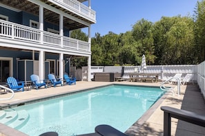 A pool with blue chairs, a table, and a covered area with a white fence.