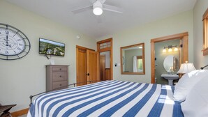 Une chambre à coucher avec un lit, une horloge, une commode, un miroir et un téléviseur fixé au mur.