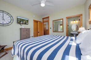 A bedroom with a bed, a clock, a dresser, a mirror, and a television on the wall.