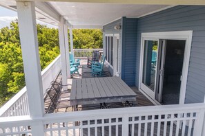 A covered outdoor deck with a table and chairs, a white railing, and a sliding glass door.