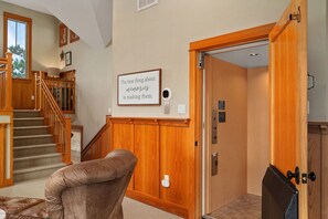 A staircase with wooden railings leading to an upper floor, a framed quote on the wall, and an elevator with a control panel.