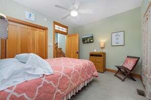 Ein Schlafzimmer mit Bett, Stuhl, Fernseher und Deckenventilator.
