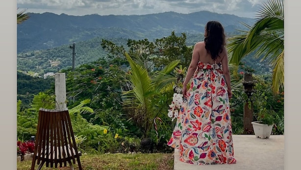 A woman in a floral dress standing on a balcony overlooking a mountainous landscape with lush greenery. - Stay in the heart of Puerto Rico in a cozy home Casa Juani - Orocovis,PR!  (Orocovis)