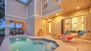 A pool area with lounge chairs and a small table, surrounded by a building with a covered patio. - Charming Retreat at Reunion | 5BR/5BA Villa, Private Pool, Arcade, Themed Kids Rooms & Golf Access (Kissimmee)