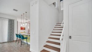 A modern interior with a staircase, a dining area with chairs, and a kitchen area. - Charming Retreat at Reunion | 5BR/5BA Villa, Private Pool, Arcade, Themed Kids Rooms & Golf Access (Kissimmee)