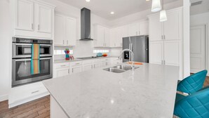 A modern kitchen with white cabinets, stainless steel appliances, and a marble island. - Charming Retreat at Reunion | 5BR/5BA Villa, Private Pool, Arcade, Themed Kids Rooms & Golf Access (Kissimmee)